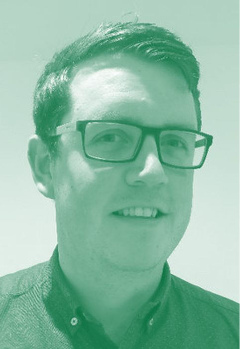 Smiling man with short dark hair and glasses wearing a dark collared shirt against a plain light background.