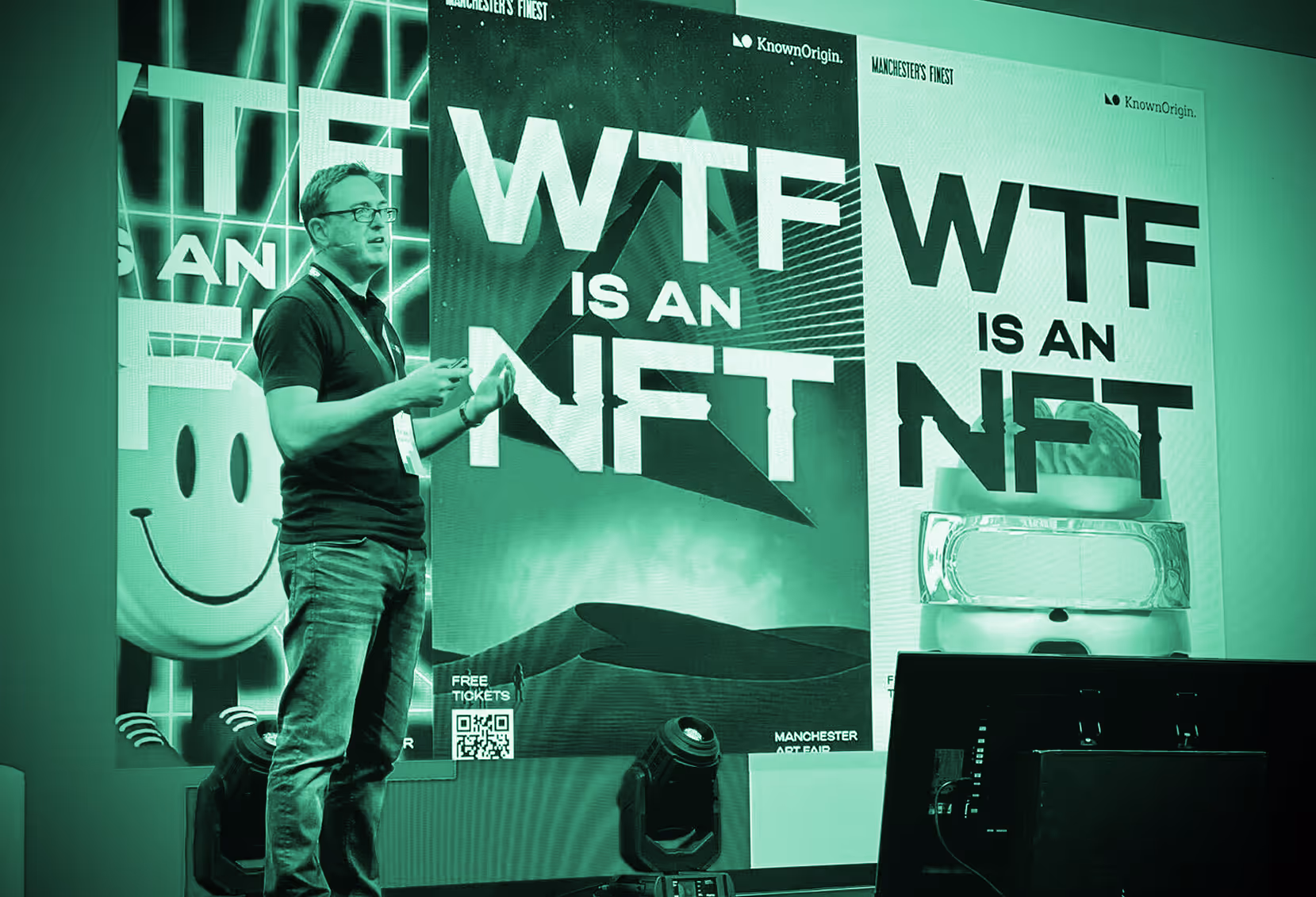 Andy Gray presenting on stage with large posters behind him asking 'WTF is an NFT' at the Manchester Art Fair.